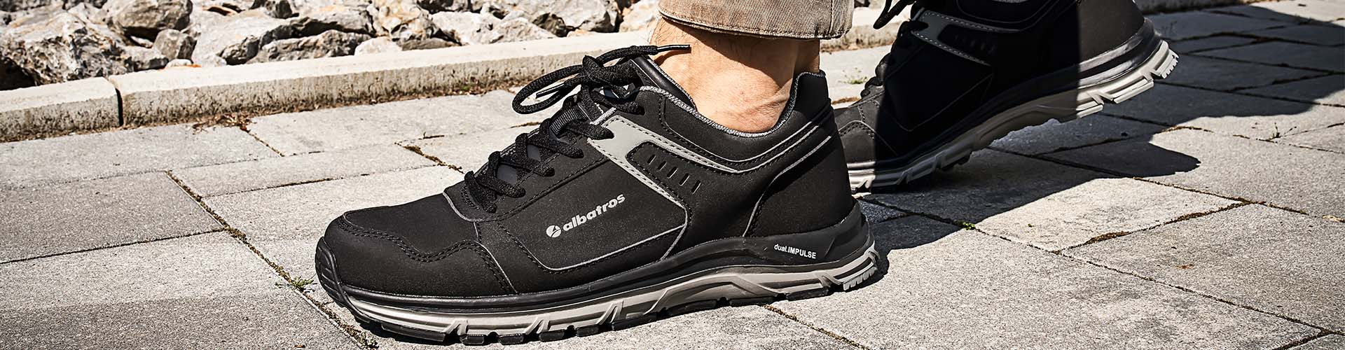 Auf dem Bild ist ein Albatros Sicherheitsschuh der Klasse O2 zu sehen, der beim Gehen auf einem gepflasterten Untergrund getragen wird.