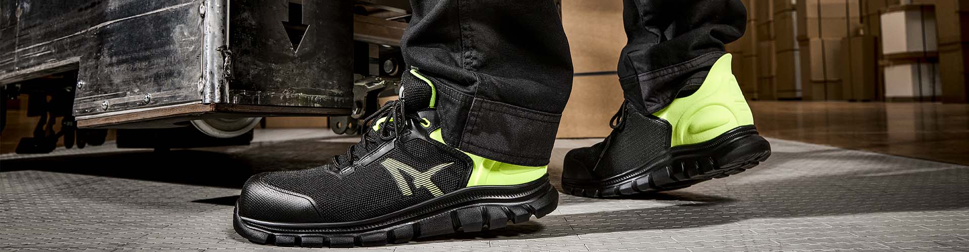 Ein Arbeiter trägt den Albatros Sicherheitsschuh OCTANE YELLOW LOW S1PS SR in Schwarz mit leuchtend gelben Elementen, während er in einer Lagerhalle arbeitet.