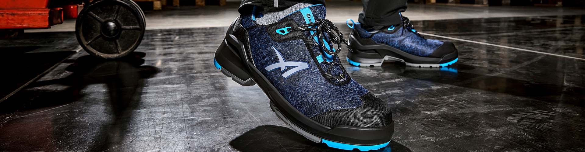 Ein Arbeiter trägt den Albatros Sicherheitsschuh TARAVAL BLUE GH LOW S3L ESD FO SR in Blau und Schwarz auf einem glänzenden Industrieboden.